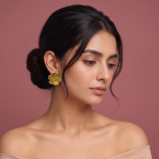 Gold plated floral stud earrings with detailed five-petal flower design worn by a woman