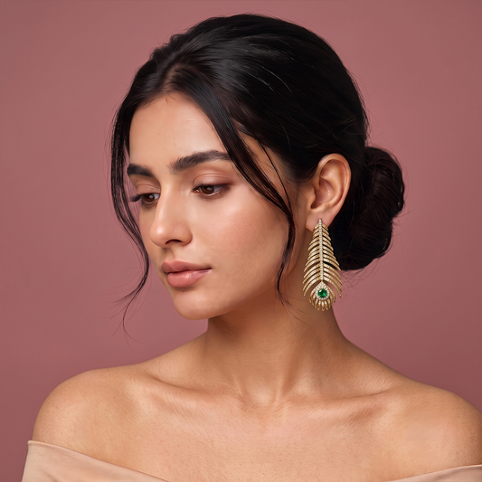 Gold plated leaf shaped drop earrings with sparkling stones and green gemstone detail worn by a woman
