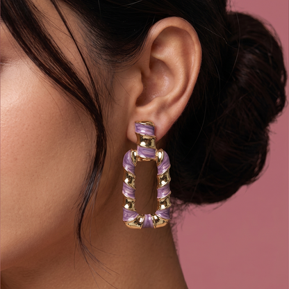 Gold plated purple enamel statement drop earrings with geometric open hoop design worn by a woman
