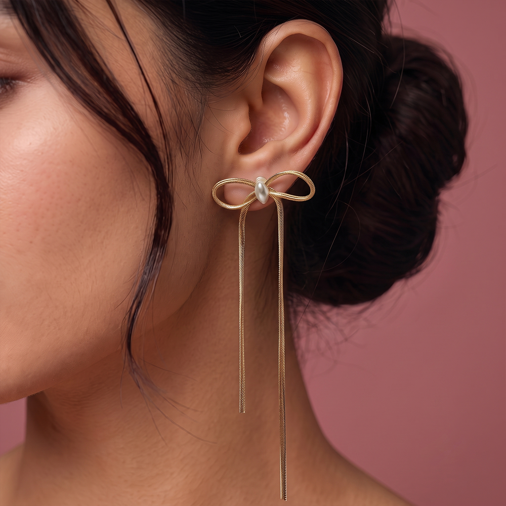 Close-up side profile of a woman wearing elegant gold bow drop earrings featuring a central pearl and long dangling chains.