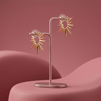 Gold plated sunburst statement stud earrings with radiating polished metal spikes displayed on a jewelry stand