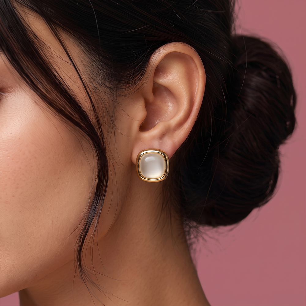 Close-up of gold plated square stud earring with luminous white pearl center worn on ear