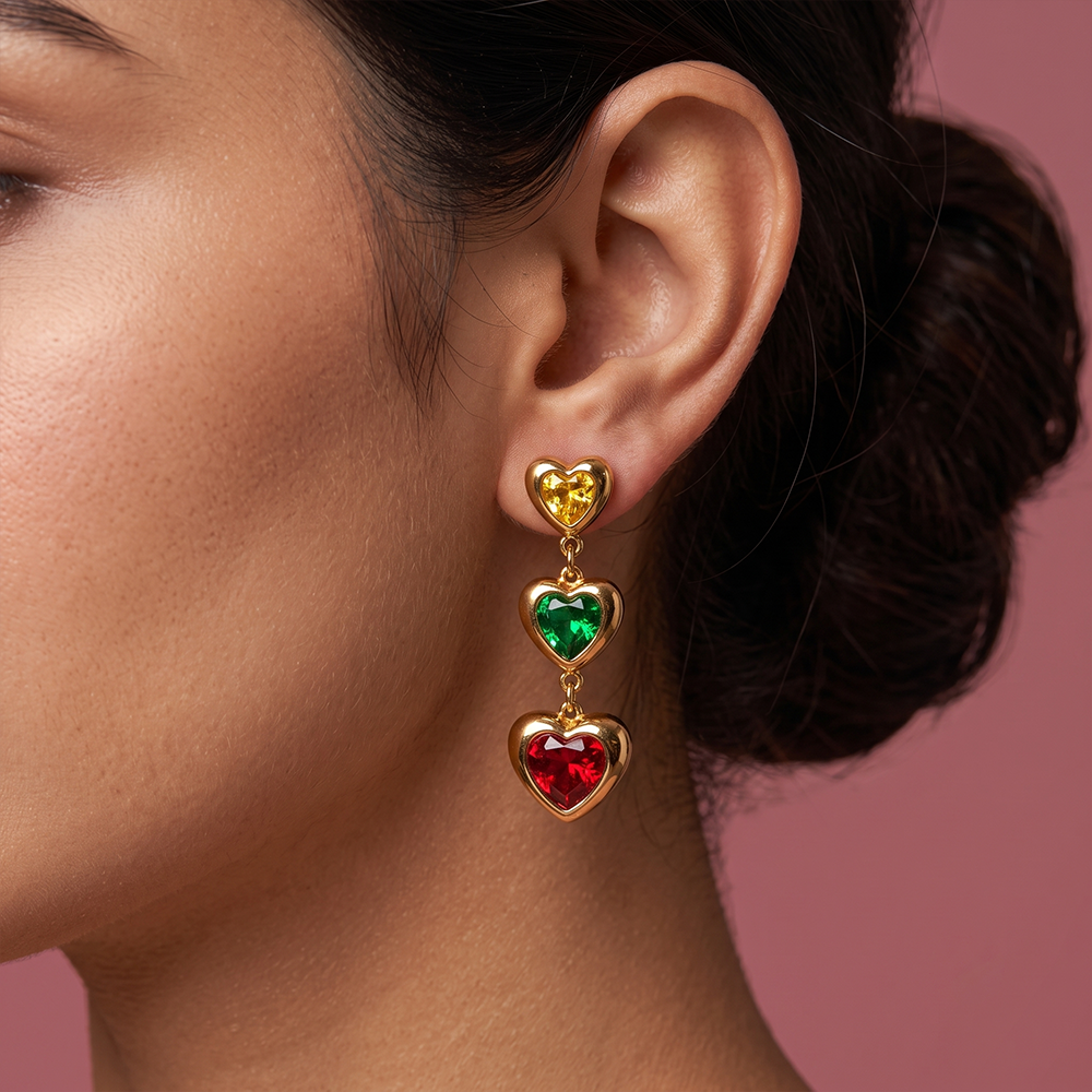 Close-up of gold plated heart shaped drop earrings with yellow, green and red gemstones