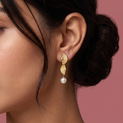 Close-up of gold plated fan shaped earrings with textured detailing, crystal accents and pearl drop worn on ear