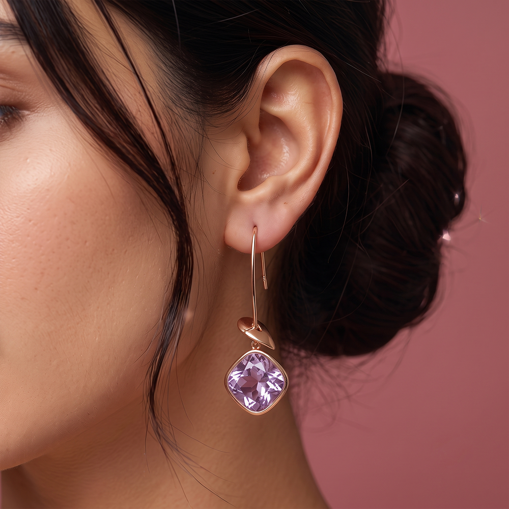 Close-up of gold plated drop earring with faceted lavender gemstone and leaf accent worn on ear