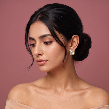 Gold plated square stud earrings with white pearl center and rounded frame worn by a woman
Image 4: