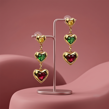 Gold plated heart drop earrings with colorful yellow, green and red heart gemstones displayed on a jewelry stand
