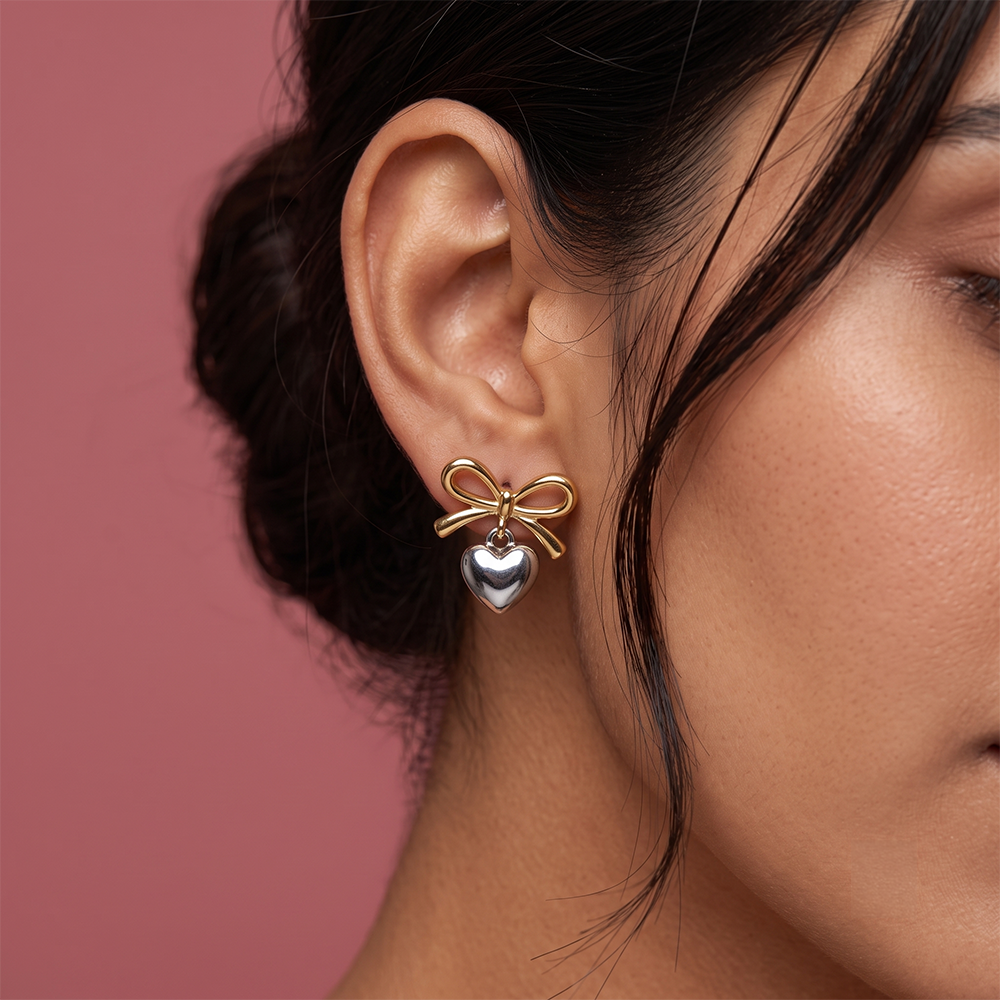 Close-up of gold-tone bow earring with a polished silver heart charm worn on a woman's ear