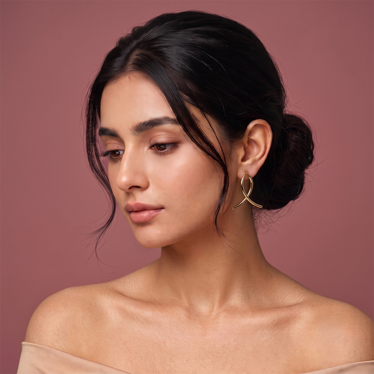 Close-up of gold plated loop earrings with smooth curved ribbon-inspired design worn on ear