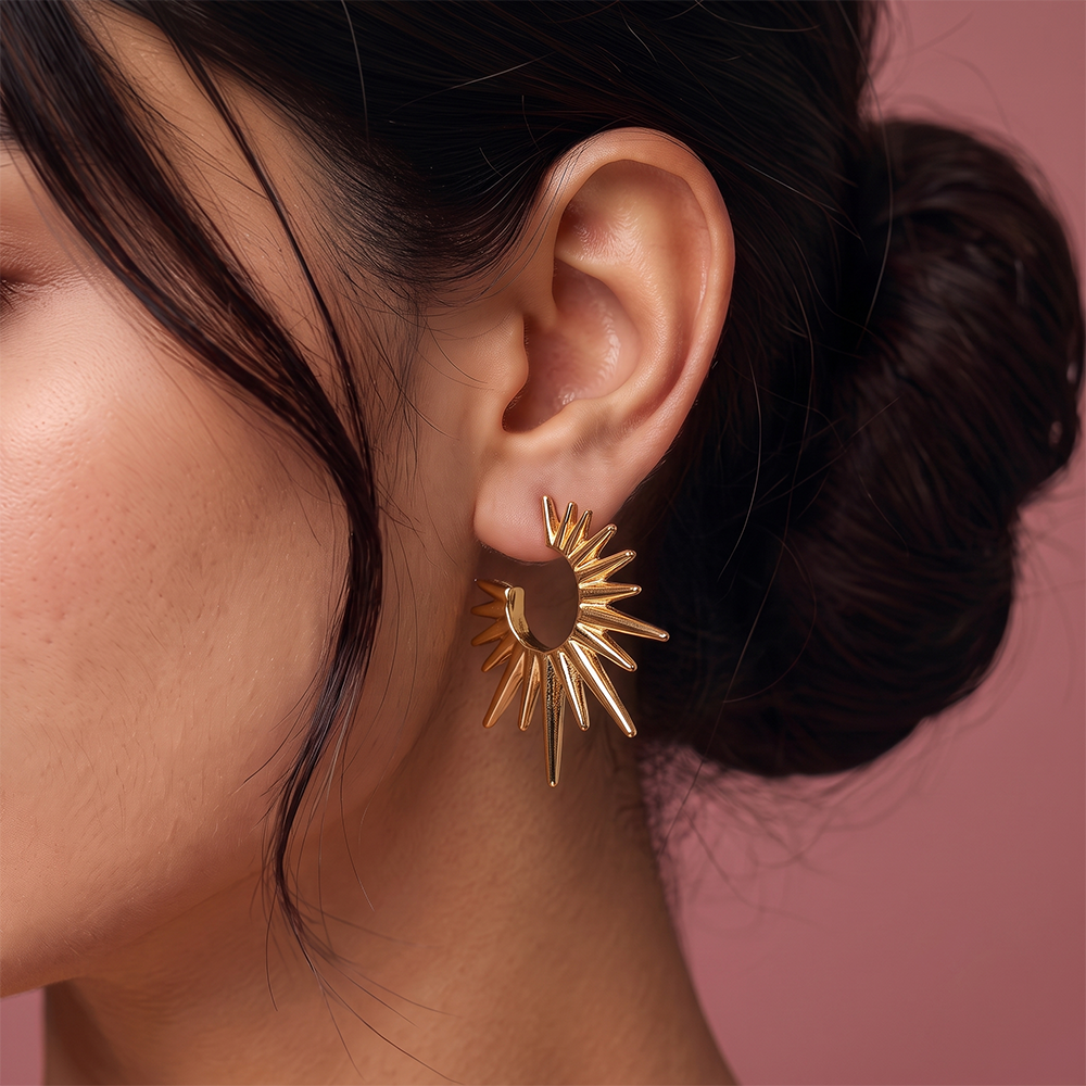 Close-up of gold plated sunburst statement earring with radiant spike design and open center worn on ear