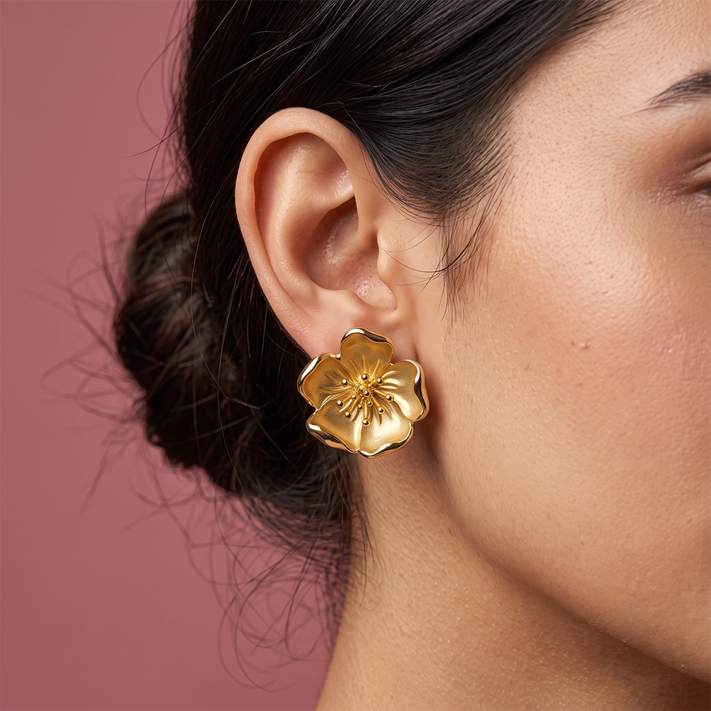 Close-up of gold plated flower stud earring with detailed petal design and textured center worn on ear